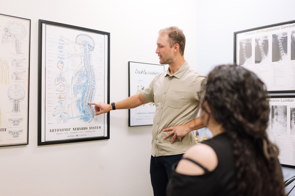 Discussing spine and nervous system anatomy during a chiropractic consultation Chiropractor explaining the autonomic nervous system to a patient using a wall chart in Mission Valley, San Diego