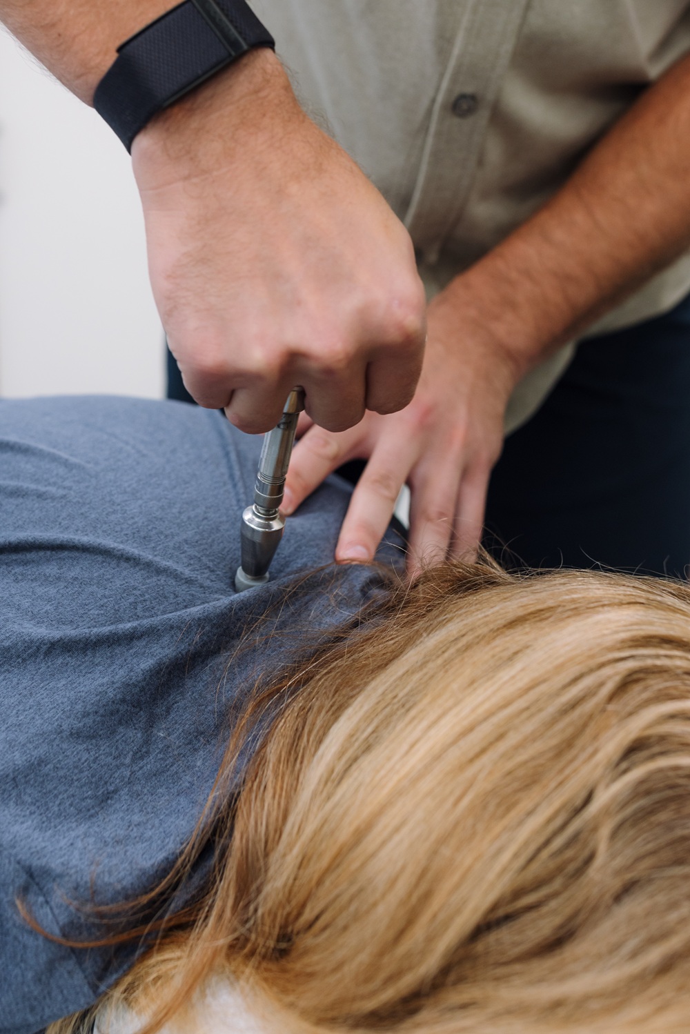Instrument-assisted adjustment for headache relief in San Diego, CA Chiropractor using a handheld adjusting instrument on a patient's upper back