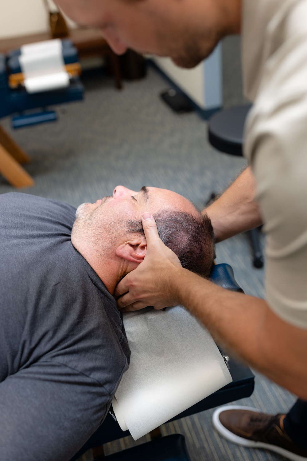 Chiropractor performing a manual neck adjustment on a patient lying on a treatment table 